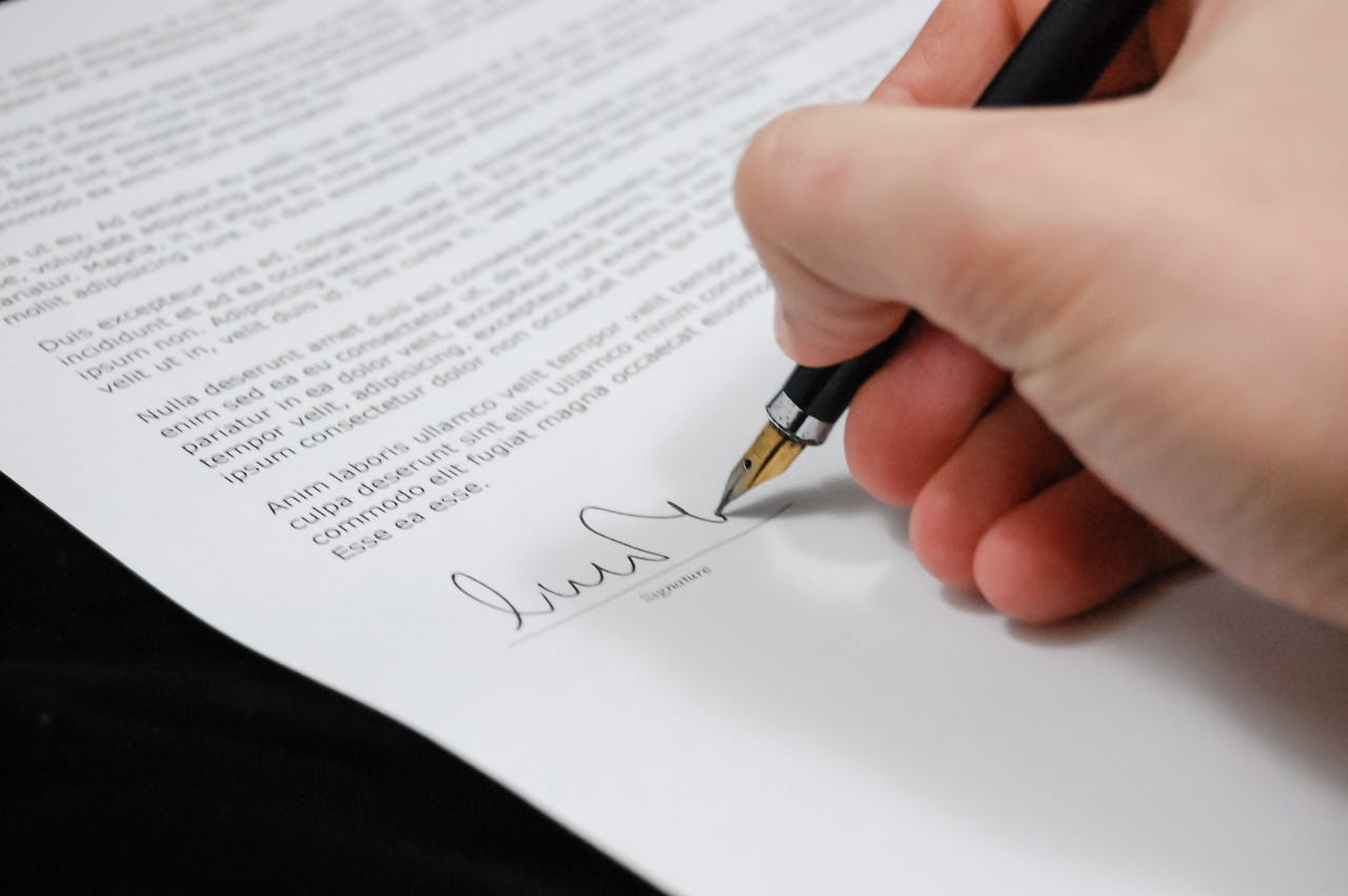 about-us-02 Close-up of a hand signing a legal document with a fountain pen, symbolizing signature and agreement.